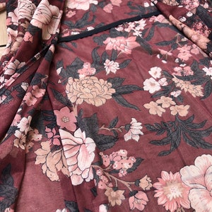 K&ouml;nnte beinhalten: Ein maroner, durchsichtiger Stoff mit einem floralen Muster in Rosa- und Beiget&ouml;nen. Der Stoff hat einen schwarzen Saum entlang der Kante.