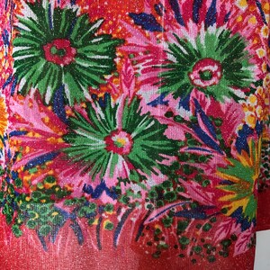 May include: Red fabric with a glittery finish and a floral print in shades of pink, green, blue, and yellow.