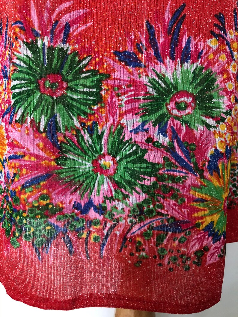 May include: Red fabric with a glittery finish and a floral print in shades of pink, green, blue, and yellow.