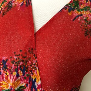 May include: Red, sparkly, floral print fabric with a V-neckline. The fabric has a subtle shimmer and a pattern of pink, yellow, green, and blue flowers.