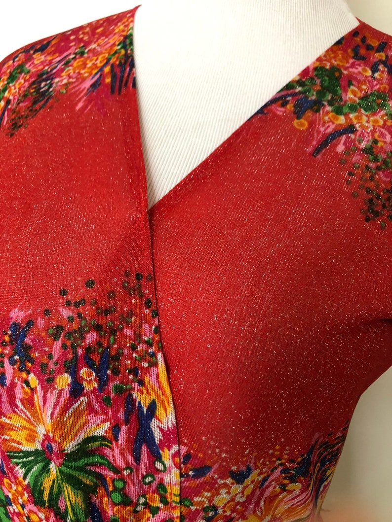 May include: Red, sparkly, floral print fabric with a V-neckline. The fabric has a subtle shimmer and a pattern of pink, yellow, green, and blue flowers.