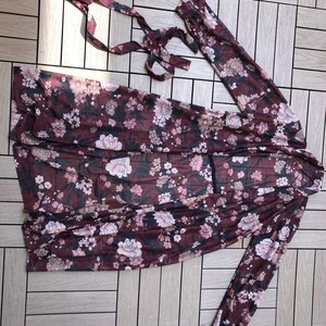 K&ouml;nnte beinhalten: Eine lang&auml;rmelige, durchsichtige Robe in Burgunderrot mit floralem Muster und einem Bindeg&uuml;rtel. Die Robe hat eine lockere Passform und ein zartes Blumenmuster.