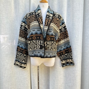 May include: A black, brown, and blue patterned cardigan with a shawl collar. The cardigan has a geometric design with stars and diamonds.