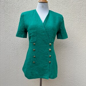 May include: A green wrap dress with short sleeves and gold buttons. The dress has a textured fabric and a v-neck.