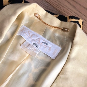 May include: A close-up of the inside of a yellow blazer with a black and gold patterned lining. The label reads "ESCA" and "MADE IN ITALY".