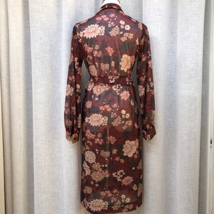 K&ouml;nnte beinhalten: Ein lang&auml;rmeliges, maronenfarbenes Kleid mit Blumendruck und einem Bindeg&uuml;rtel. Das Kleid ist durchsichtig und hat eine lockere Passform.