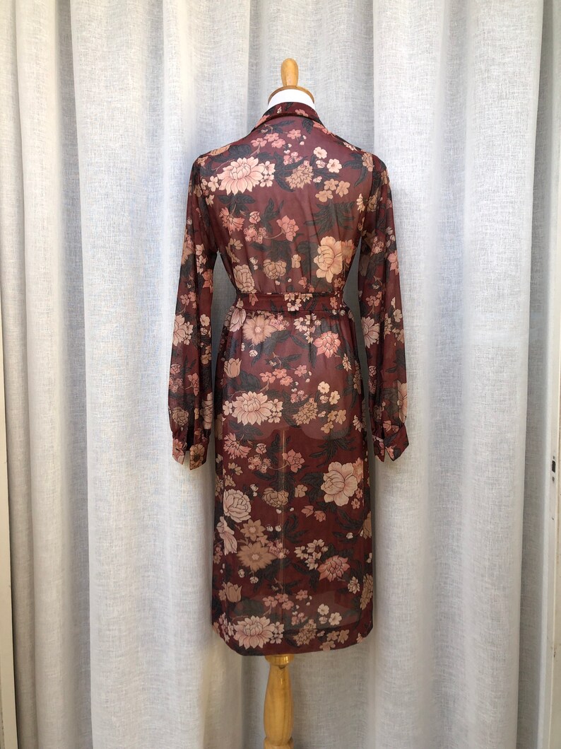 K&ouml;nnte beinhalten: Ein lang&auml;rmeliges, maronenfarbenes Kleid mit Blumendruck und einem Bindeg&uuml;rtel. Das Kleid ist durchsichtig und hat eine lockere Passform.