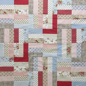 May include: A patchwork quilt featuring a repeating pattern of rectangular fabric strips. The design incorporates various prints including red and white gingham, blue and white checks, pink stripes, and floral motifs in shades of red, green, and blue.