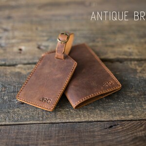 May include: Two brown leather luggage tags with the initials "JRC" embossed on them. The tag on the left has a brass loop for attaching to luggage. The text "ANTIQUE BROWN" is visible at the top of the image.