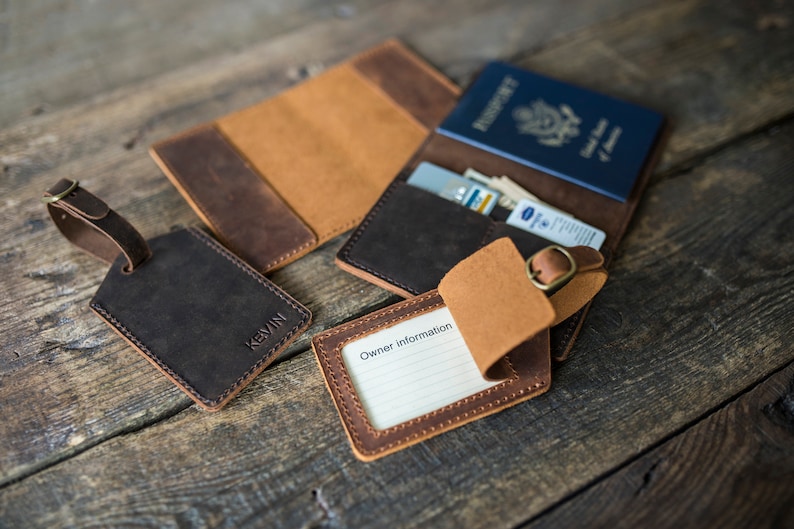 May include: Two brown leather luggage tags with a brass buckle, one with the name "Kevin" embossed on it, and the other with a blank space for "Owner Information". A brown leather passport holder with a blue passport inside.
