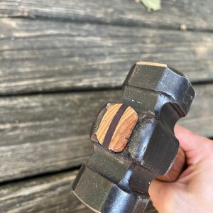 May include: A black metal hammer with a wooden handle. The hammer head has a flat striking surface and a rounded face. The handle is wrapped in brown leather.
