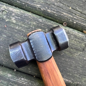 May include: A black metal hammer with a wooden handle. The hammer has a rounded head with a flat striking surface.
