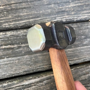 May include: A black and silver hammer with a wooden handle. The hammer head has a hexagonal shape and the text "BLD" is stamped on the side.