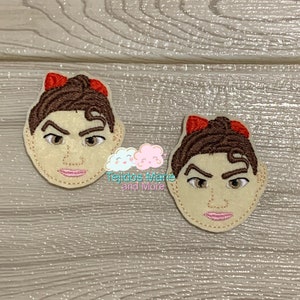 May include: Two embroidered felt patches of a cartoon face with brown hair, brown eyes, and a red bow. The face has a neutral expression.