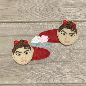 May include: Two red felt hair clips with a cartoon face embroidered on each. The face has brown hair, brown eyes, and a light brown complexion.