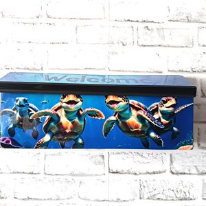 May include: A blue mailbox with a black roof featuring a vibrant underwater scene with cartoon sea turtles. The word "Welcome" is printed on the top of the mailbox.