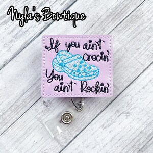 May include: A pink fabric badge holder with a blue and white cartoon shoe and the text "If you ain't crectin' you ain't rockin'".