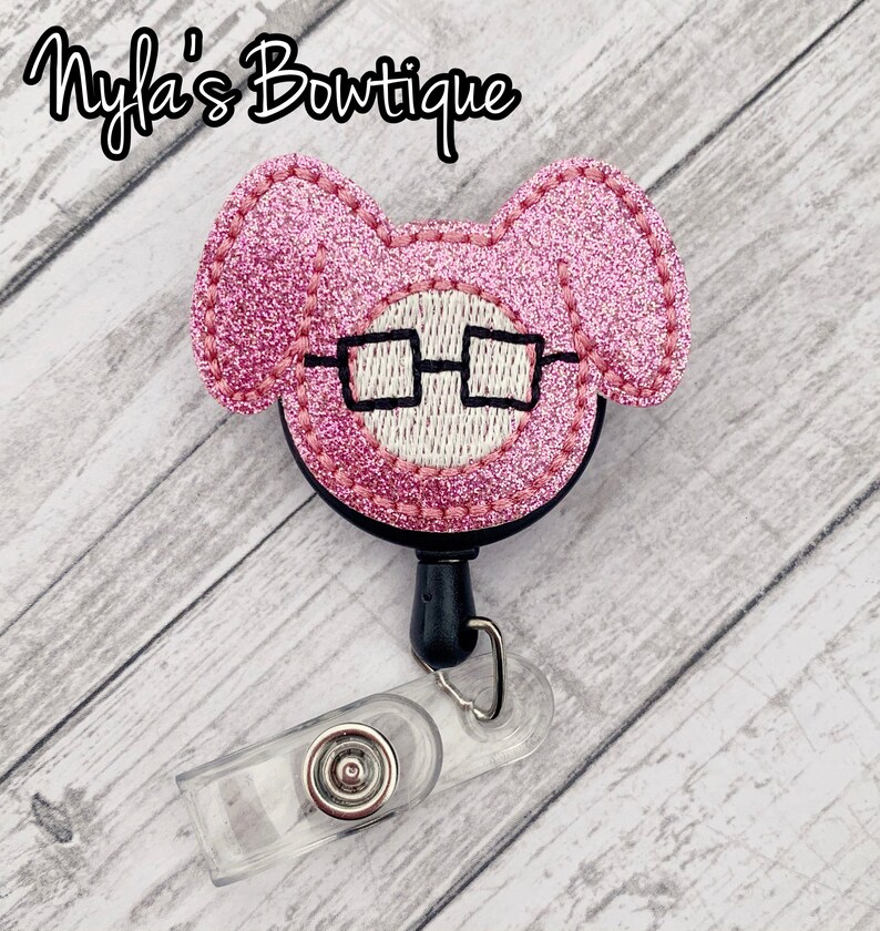 May include: Pink glitter mouse with black glasses, attached to a black retractable badge reel with a clear plastic badge holder.