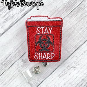 May include: Red glitter badge holder with a red and white biohazard symbol and the text "Stay Sharp".