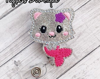 May include: Silver glitter mermaid cat badge reel with a pink tail and a purple star on its head.  The reel is clear plastic with a silver metal clip.
