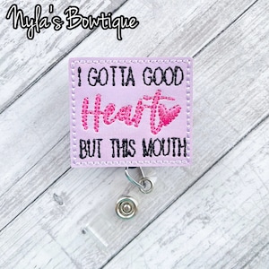 May include: A purple fabric badge holder with the text "I gotta good heart but this mouth" in black and pink lettering. The badge holder has a clear plastic clip.