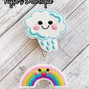 May include: A white glitter cloud with a blue outline and a smiling face, with blue raindrops falling from it, attached to a rainbow with a smiling face. The cloud and rainbow are both attached to a clear plastic badge holder.