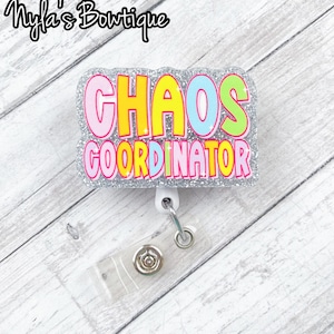 May include: A silver glitter badge holder with a white retractable reel. The badge holder has the text "CHAOS COORDINATOR" in colorful letters.