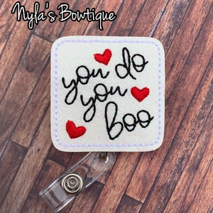 May include: White glitter badge holder with a black embroidered design that says "you do you boo" with three red hearts.