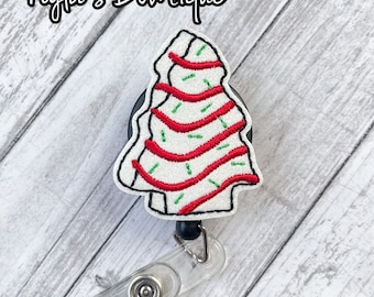 Könnte beinhalten: Weißer Weihnachtsbaum-förmiger Badge-Rollenhalter mit roten und grünen Stickereien. Der Rollenhalter ist an einem durchsichtigen Plastik-Badge-Halter befestigt.
