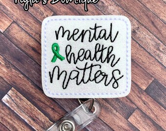 May include: White square badge holder with a green ribbon and the text "mental health matters" in black cursive lettering. The badge holder is attached to a clear plastic retractable badge reel.