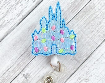 May include: A light blue castle-shaped badge holder with a white and clear retractable reel. The castle is decorated with pink, green, and blue polka dots.