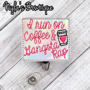 May include: A white and iridescent badge holder with a pink embroidered design that says "I run on coffee & gangsta rap" with a coffee cup graphic. The badge holder has a clear plastic retractable clip.