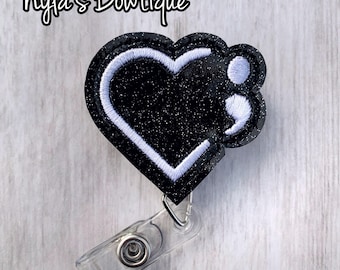May include: Black glitter heart-shaped badge holder with a white outline and a white semicolon symbol. The badge holder is attached to a clear plastic retractable badge reel.