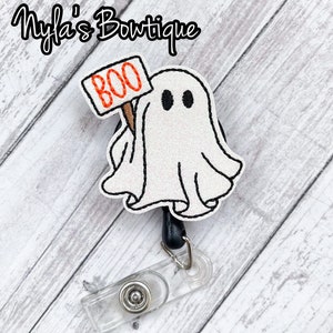 May include: A white ghost with black eyes holding a sign that says "BOO" on a black retractable badge reel.