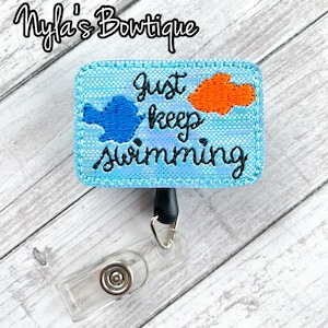 May include: A blue and orange embroidered badge holder with the text "Just keep swimming".