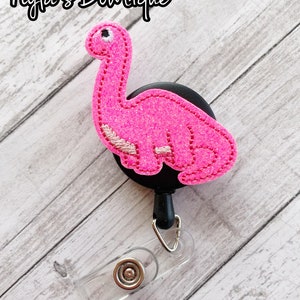 May include: Pink glitter dinosaur badge reel with a black swivel clip and a clear badge holder.