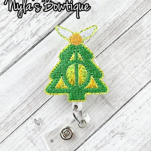 May include: Green Christmas tree-shaped badge holder with a gold glitter Deathly Hallows symbol and a white and gold glitter winged snitch on top.
