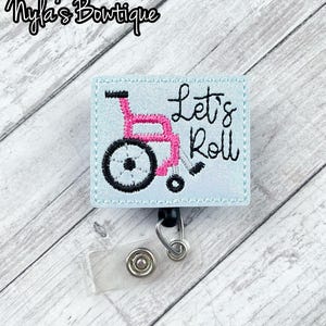 May include: A light blue badge holder with a white embroidered wheelchair and the text "Let's Roll".