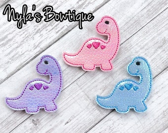 May include: Three felt dinosaur appliques with pink, purple, and blue iridescent finishes. Each dinosaur has a pink heart design on its back.