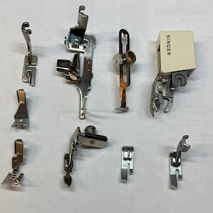 May include: A collection of nine silver sewing machine feet, including a foot with the word "SINGER" on it.