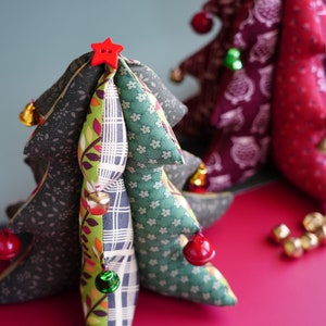 May include: Two handmade fabric Christmas trees with red and green accents. The smaller tree is red and white with a star on top. The larger tree is green, brown, and white with a red star on top. Both trees have bells and ornaments.