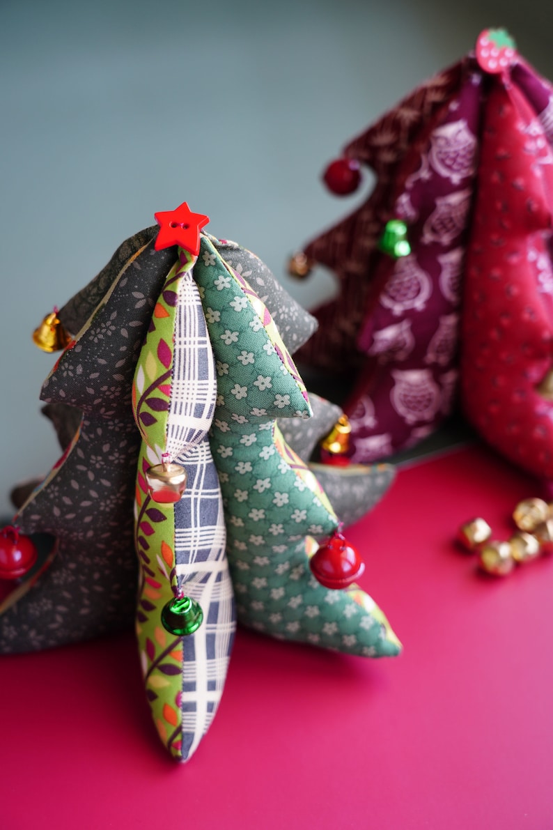 May include: Two handmade fabric Christmas trees with red and green accents. The smaller tree is red and white with a star on top. The larger tree is green, brown, and white with a red star on top. Both trees have bells and ornaments.