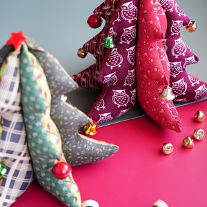 May include: Two handmade fabric Christmas trees, one with a red and white owl print and the other with a green and brown plaid print. Both trees have bells and red berries. There are also spools of thread on a pink surface.