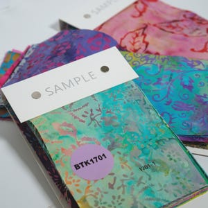 May include: A stack of fabric swatches featuring batik patterns in vibrant shades of teal, green, pink, and purple. Each swatch set is topped with a white header card labelled SAMPLE and a circular purple sticker with the text BTK1701 and 1701-1.