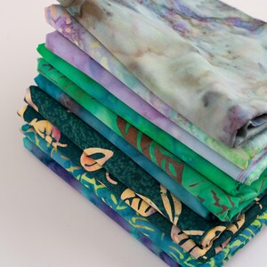 May include: A stack of 10 fabric squares in various shades of green and purple. The fabric squares have different patterns, including floral and geometric designs.