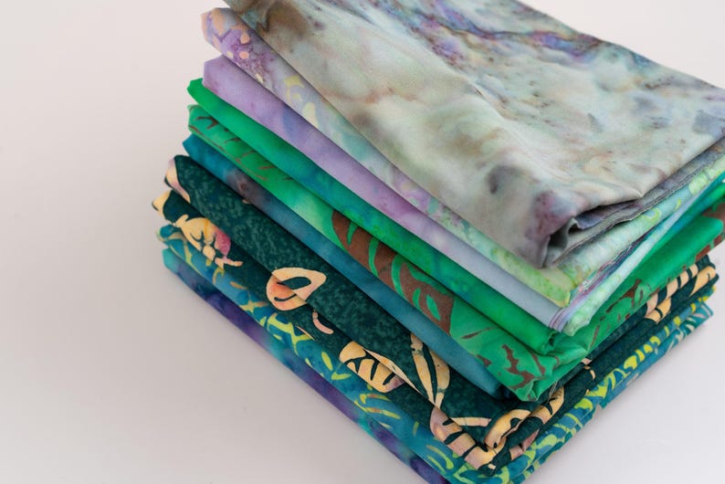 May include: A stack of 10 fabric squares in various shades of green and purple. The fabric squares have different patterns, including floral and geometric designs.