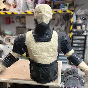May include: A black and gray costume piece with a textured surface. The costume piece is made of foam and is being assembled on a mannequin.