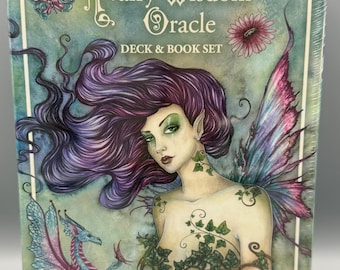 May include: A boxed "Fairy Wisdom Oracle Deck & Book Set" features a watercolor illustration of a fairy with purple hair, ivy, and butterfly wings. The box has the text "Fairy Wisdom Oracle" and the names "Amy Brown" and "Nancy Brown".