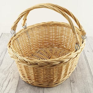 May include: A natural woven wicker basket with two handles. The basket is oval shaped and has a light brown colour.