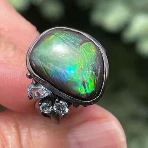 May include: A silver ring with a large, iridescent green gemstone and three smaller, clear gemstones.